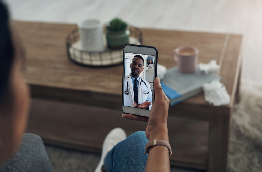 A woman holds her phone and speaks with her doctor on a virtual call